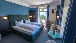 A hotel room with a large bed, a small table with a vase of flowers, a chair, and a balcony with outdoor seating. - Hotel Royal Lucerne (Lucerne)
