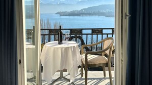 A balcony with a table and chair, overlooking a lake and mountains. - Hotel Royal Lucerne (Lucerne)