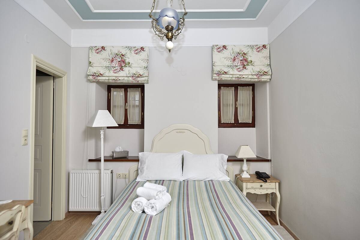 A bedroom with a bed, two bedside tables, a nightstand, a radiator, a ceiling light fixture, and a door.