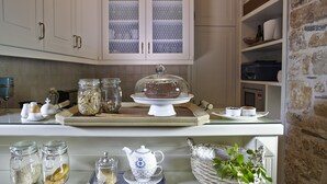 Una cocina con armarios blancos, un aparador con puerta de vidrio, un pastel sobre un pedestal y varios utensilios de cocina sobre la encimera.