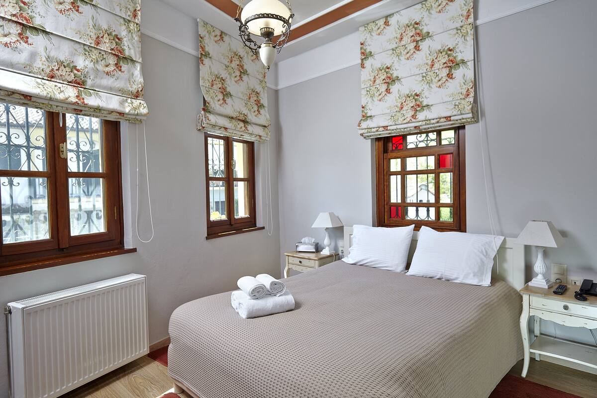 A neatly arranged bedroom with a large bed, two bedside tables, a nightstand, and a radiator.