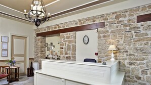 Zona de recepción con pared de piedra, mostrador blanco, candelabro y un reloj en la pared.