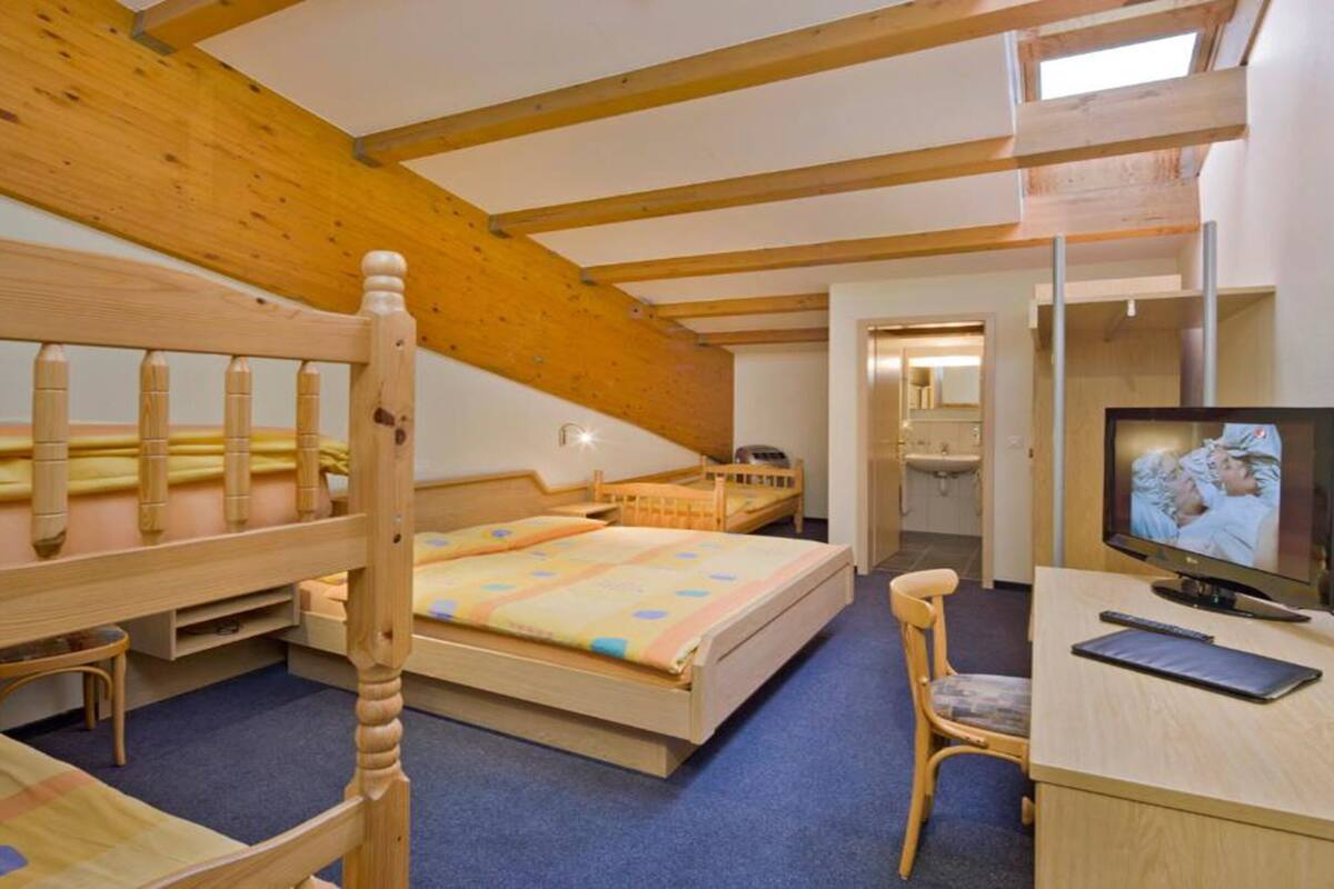 A room with two bunk beds, a desk with a chair, a television, and a bathroom visible through an open door.