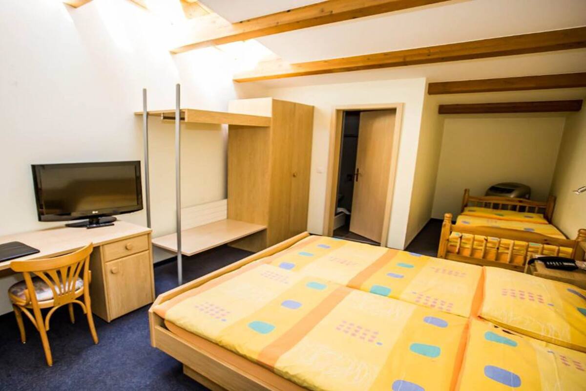 A bedroom with a bed, a desk with a computer, a chair, and a television.