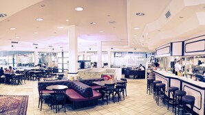 A spacious restaurant with high ceilings, multiple seating areas including booths and tables, a bar area, and a visible kitchen. - Hotel Olympica (Brig)