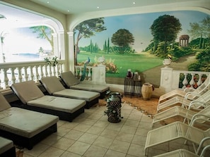 Una habitación soleada con sillones de descanso, una urna decorativa y un mural de un campo de golf.
