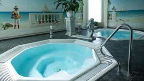 A luxurious indoor pool area with a large hot tub, decorative statues, and a mural depicting a beach scene. - Hotel Olympica (Brig)