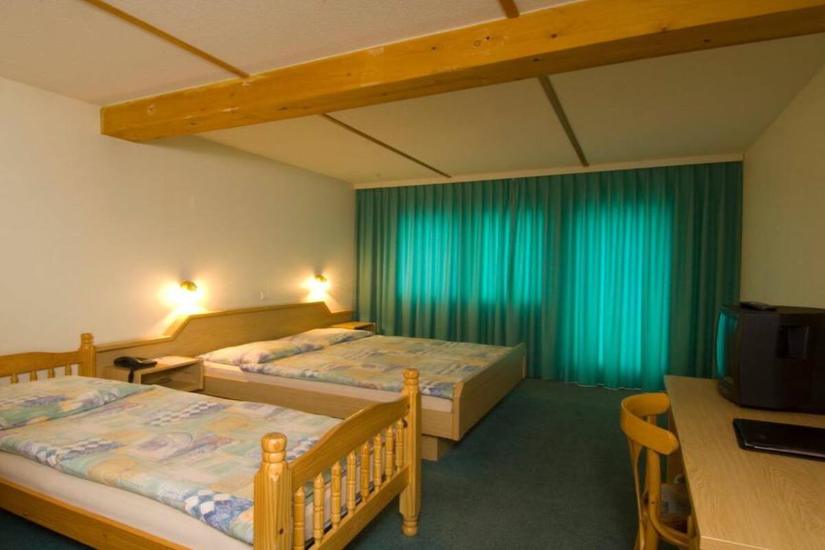 A room with two wooden beds, a desk, a chair, a television, and a curtain.