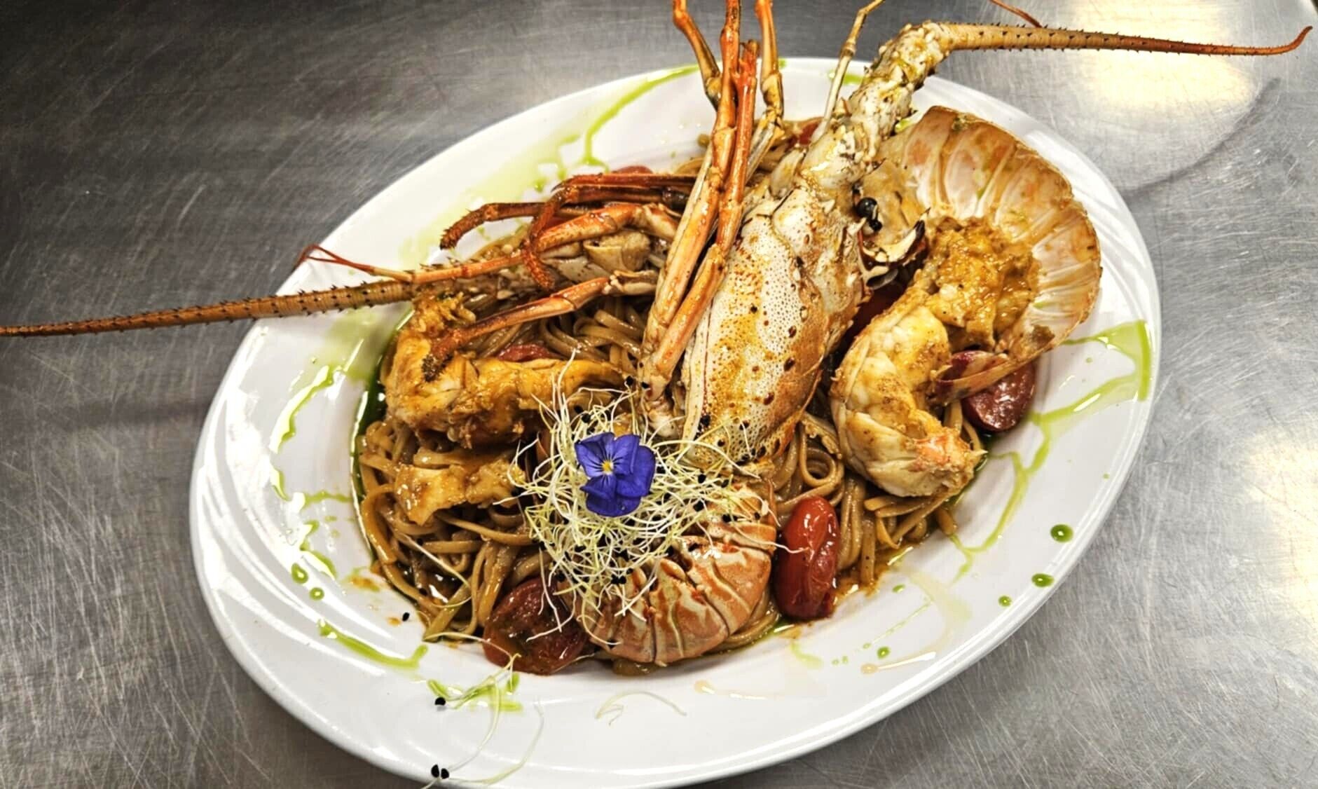 Une assiette de nourriture comprenant un homard, des pâtes et une garniture florale.