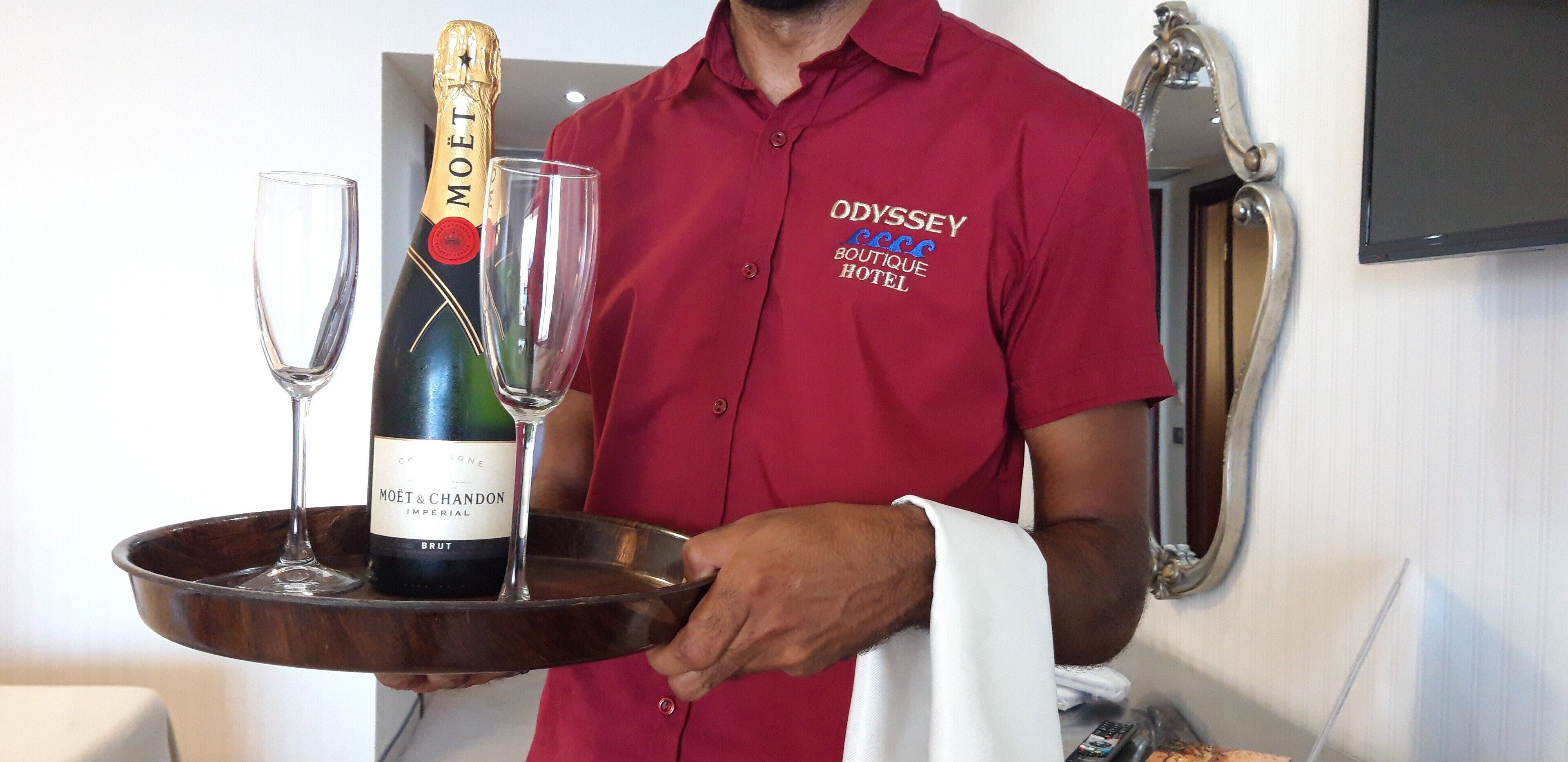 A person in a red shirt holding a tray with a bottle of Moët & Chandon champagne and two glasses.