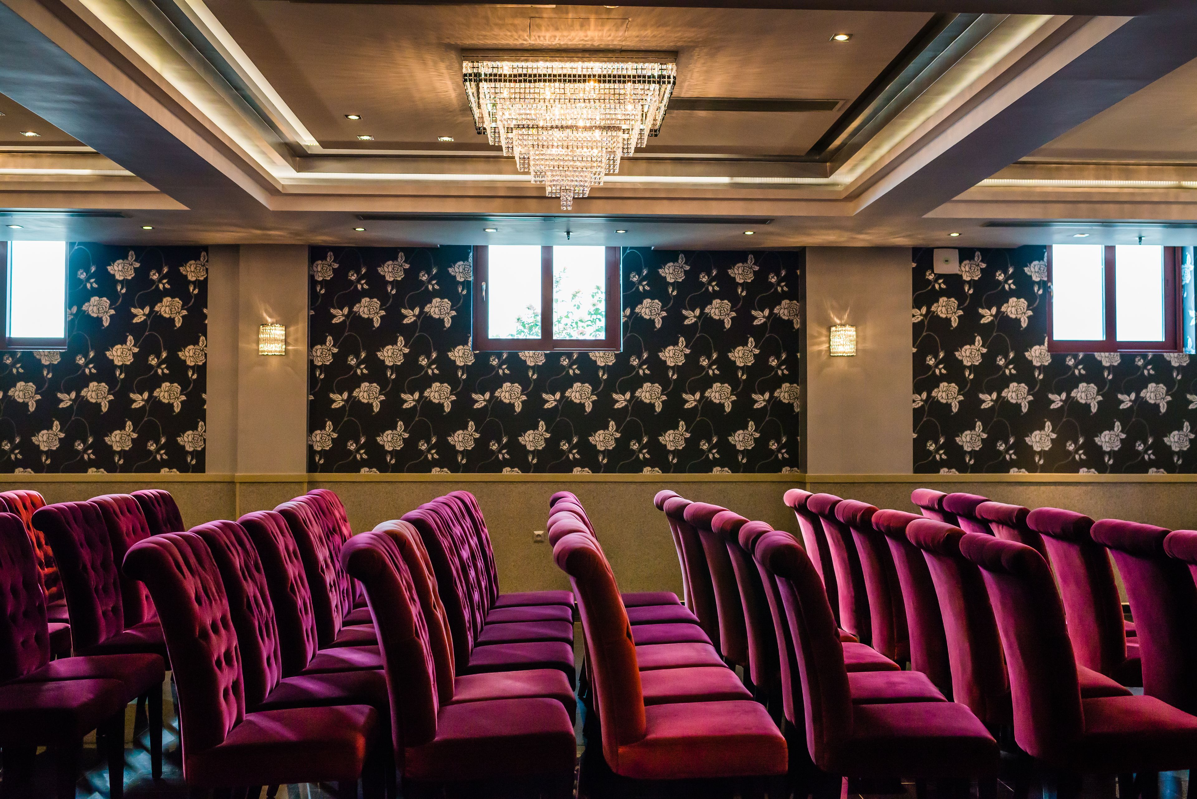 Rows of purple upholstered chairs in a room with floral wallpaper and a chandelier.