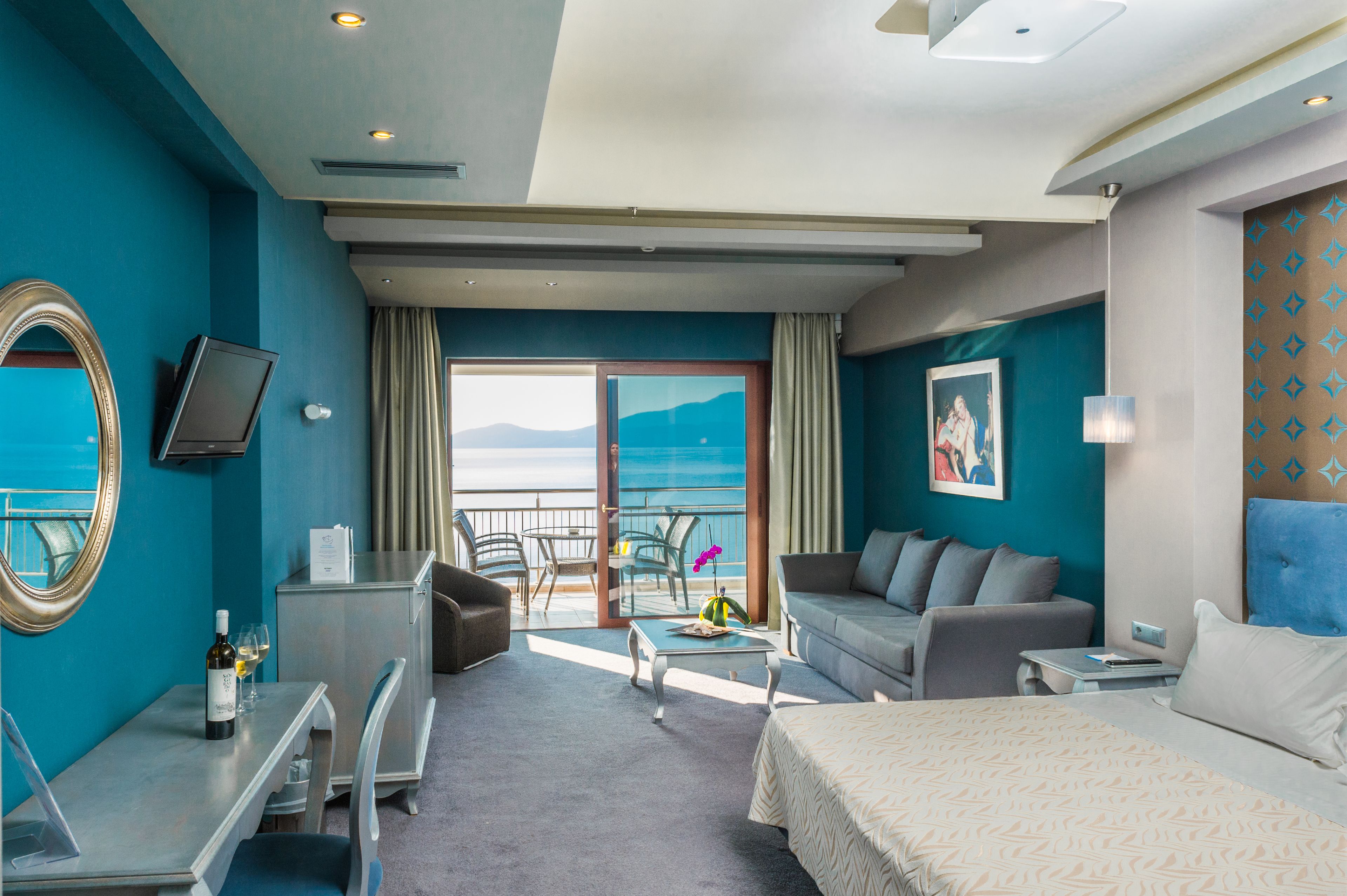 Una habitación de hotel con cama, sofá, escritorio y balcón con vista al mar.