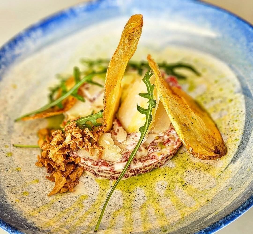 A plate of food with a creamy base, topped with crispy elements and greens.