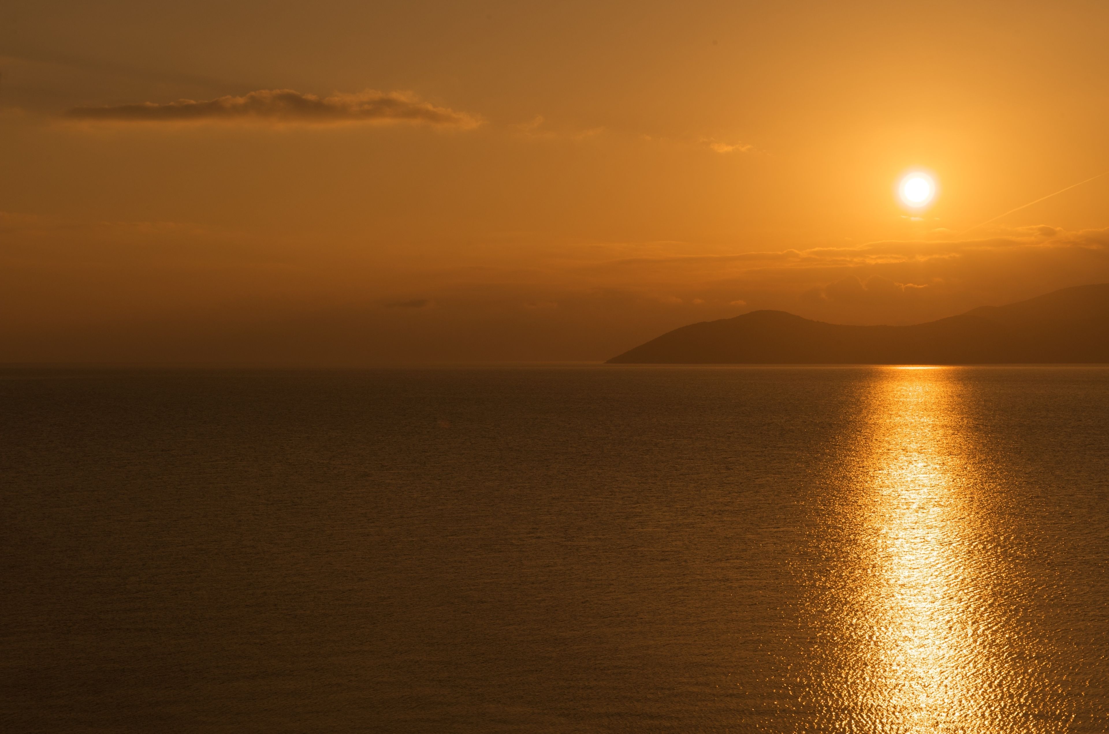Ein Sonnenuntergang über einem ruhigen Meer mit einem fernen Berg.