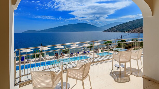 A balcony with a pool, white chairs, and umbrellas, overlooking a body of water and mountains. - Odyssey Boutique Hotel (Kefalonia)