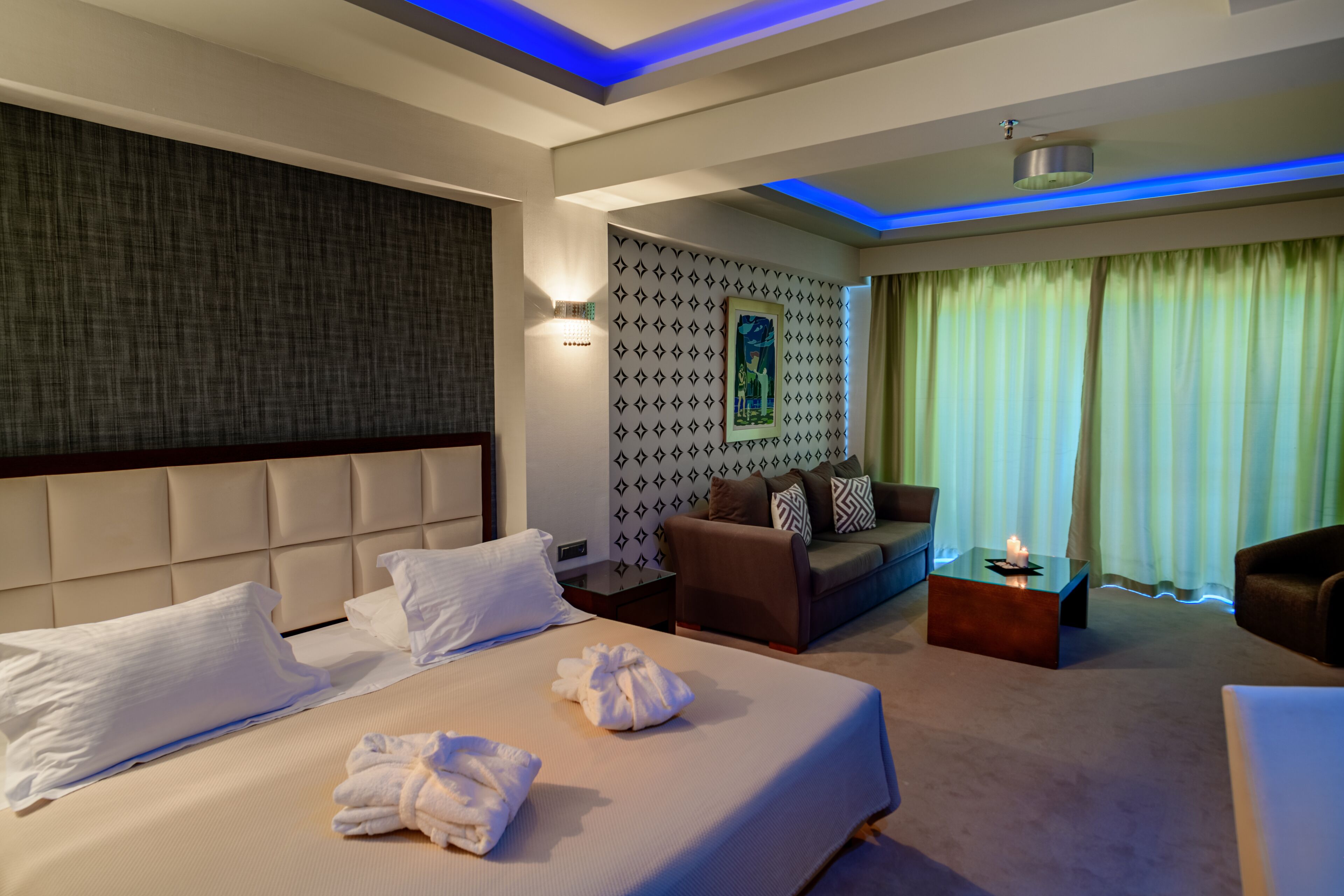 Een hotelkamer met een groot bed, een bank, een klein bijzettafeltje en een wand met een geometrisch patroon.