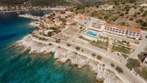 An aerial view of a coastal resort with a swimming pool, buildings, and a marina. - Odyssey Boutique Hotel (Kefalonia)