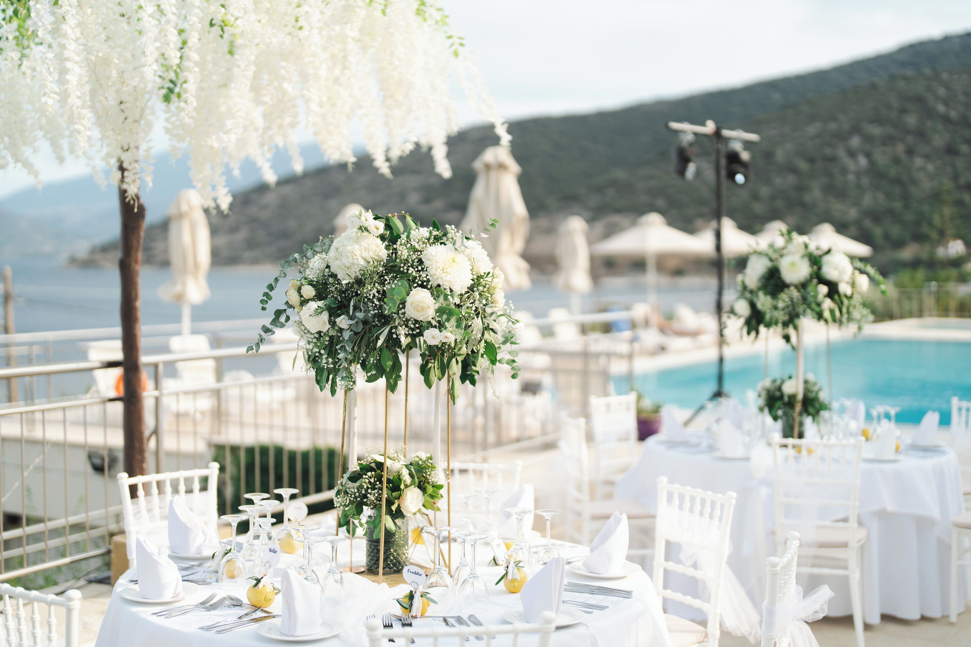 A table set for a formal event with white tablecloths, glassware, and a floral centerpiece.