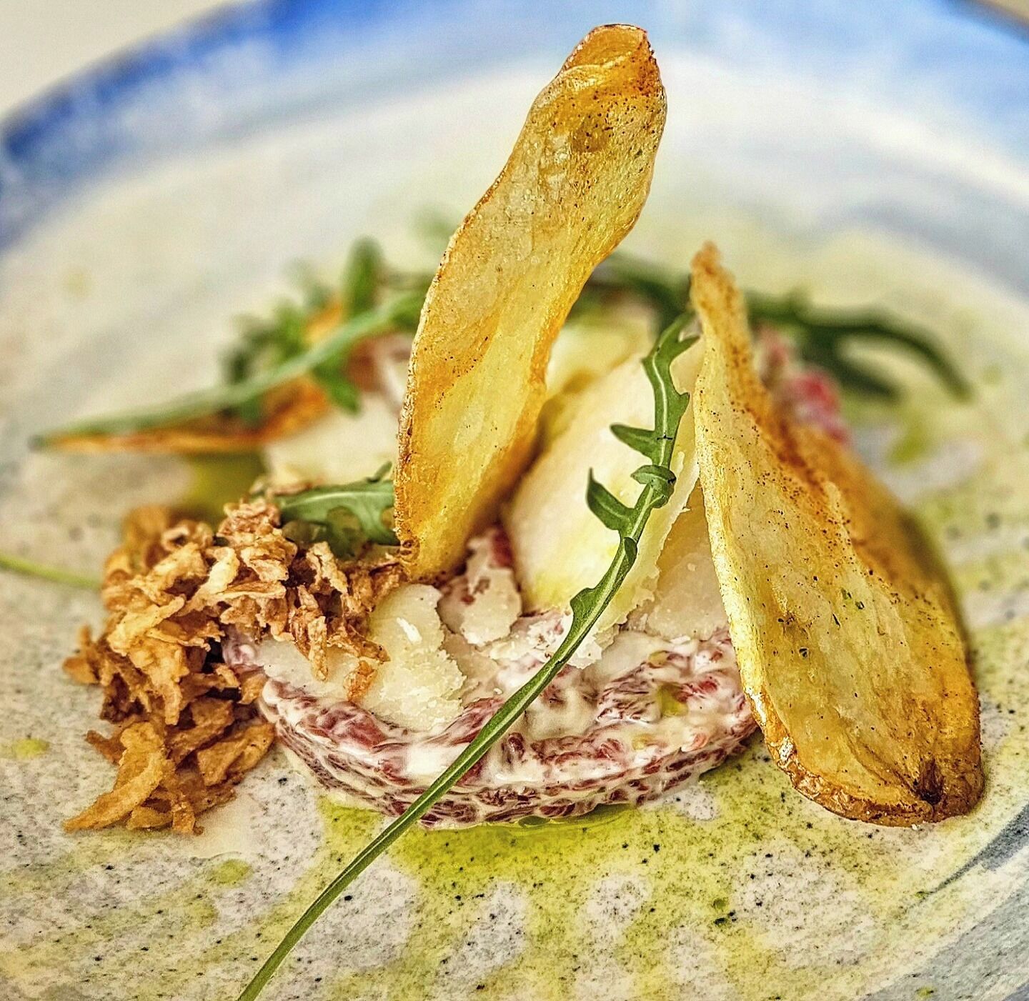 A dish with a creamy base, garnished with greens and crispy elements.