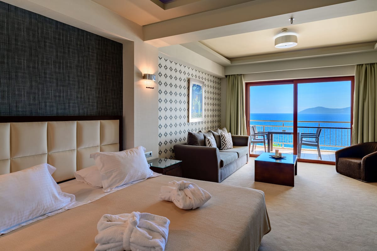Une chambre d’hôtel avec un grand lit, un canapé, un bureau et un balcon donnant sur la mer.