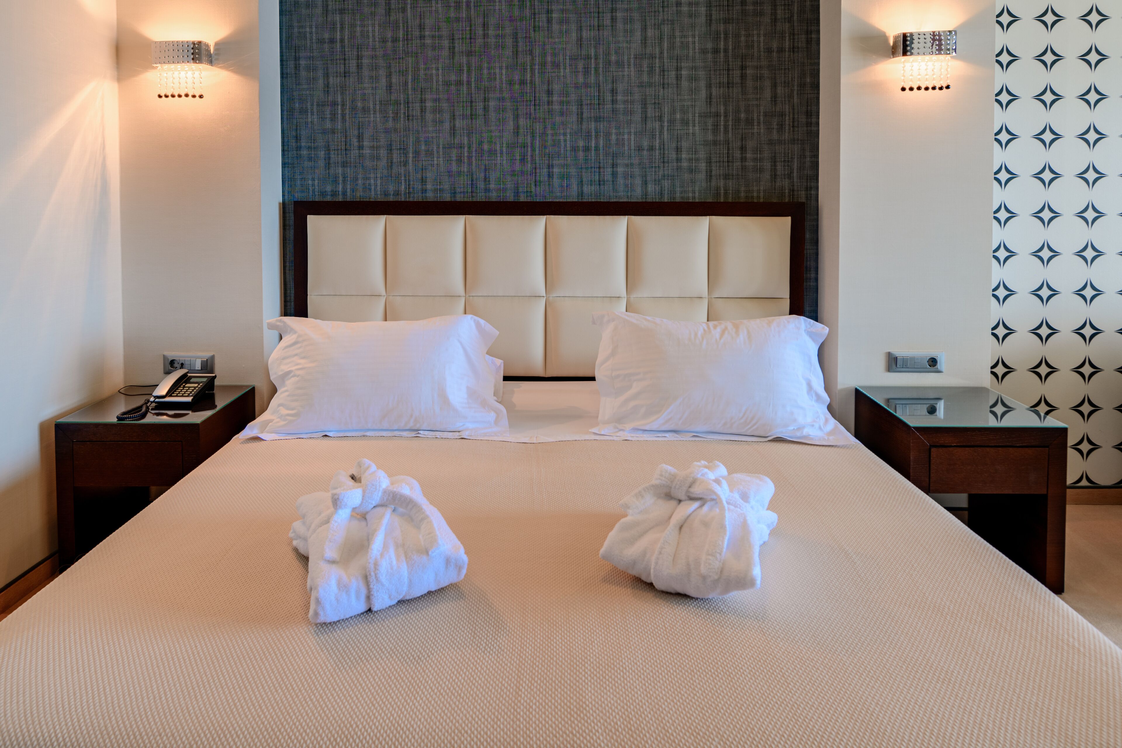 A hotel room with a large bed, two bedside tables, a telephone, and two towels on the bed.