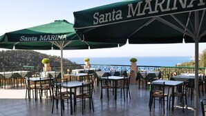 Outdoor seating with 'Santa MARINA' umbrellas, tables, and chairs, overlooking a scenic view.