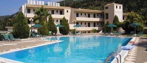 A swimming pool with a tiled deck, lounge chairs, and umbrellas.