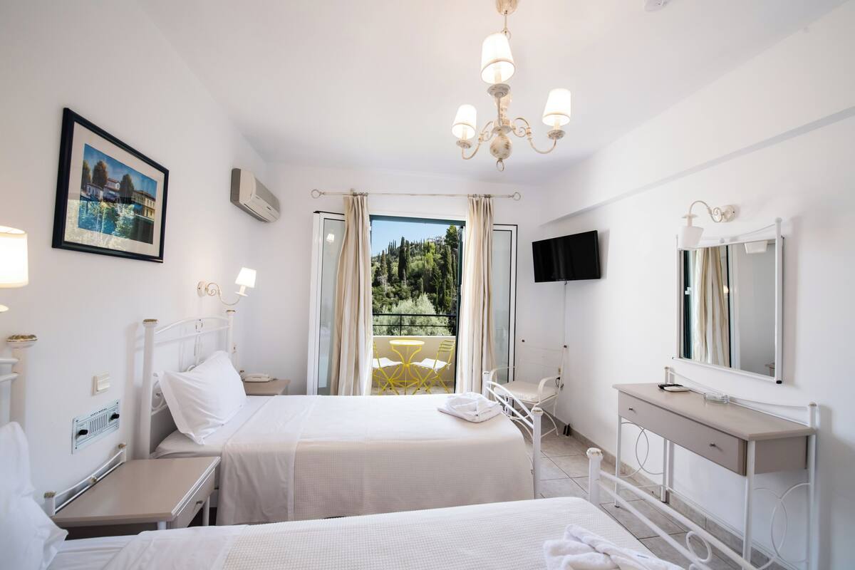 Ett hotellrum med två sängar, ett skrivbord, en stol, en TV och en balkong med utsikt.