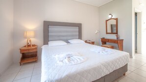 A hotel room with a large bed, a bedside table with a lamp, a wooden dresser, and a mirror on the wall. - Anamar Zante Hotel (Zakynthos)