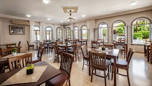 A spacious dining area with multiple tables and chairs, large arched windows, and a ceiling fan. - Anamar Zante Hotel (Zakynthos)