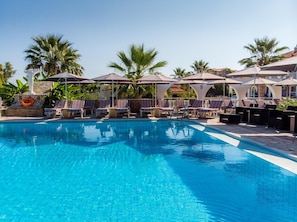 A pool area with lounge chairs and umbrellas, surrounded by palm trees. - Anamar Zante Hotel (Zakynthos)