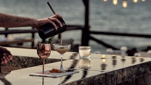 A person pouring a drink into a glass at a bar with a view of the sea. - Windmill Bay Hotel (Zakynthos)