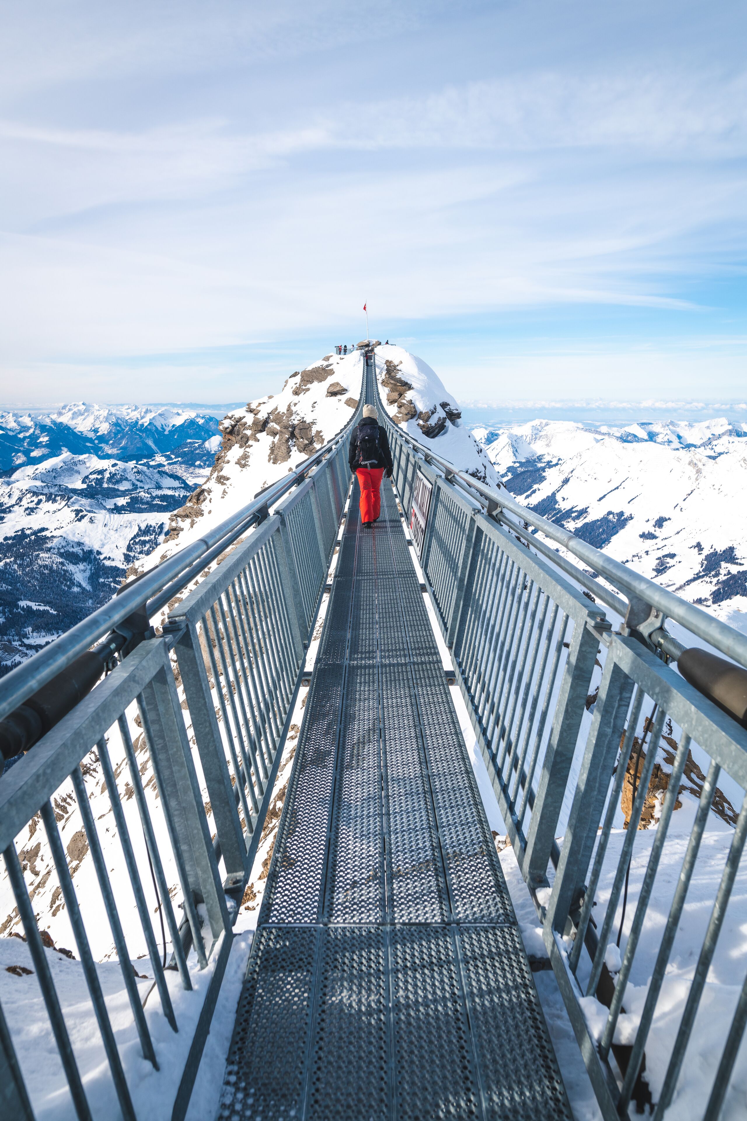 Un puente de metal con barandillas, que conduce a la cima nevada de una montaña.