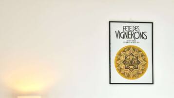 Un lit bien fait, avec une literie blanche et grise, une œuvre d’art encadrée au mur et une lampe de chevet sur une table de nuit.
