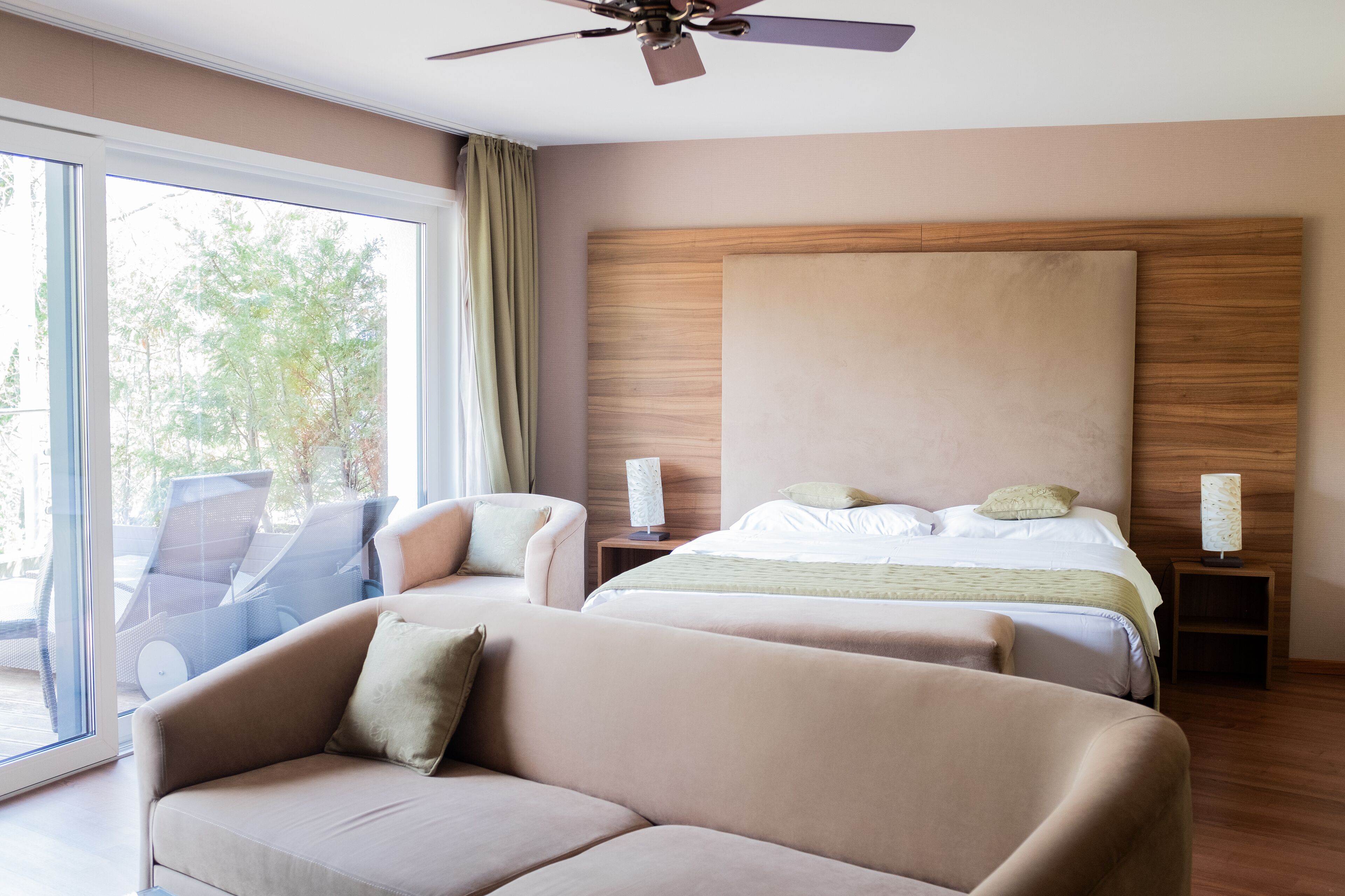 A hotel room with a large bed, two bedside tables, a ceiling fan, and a seating area with a sofa and chairs.