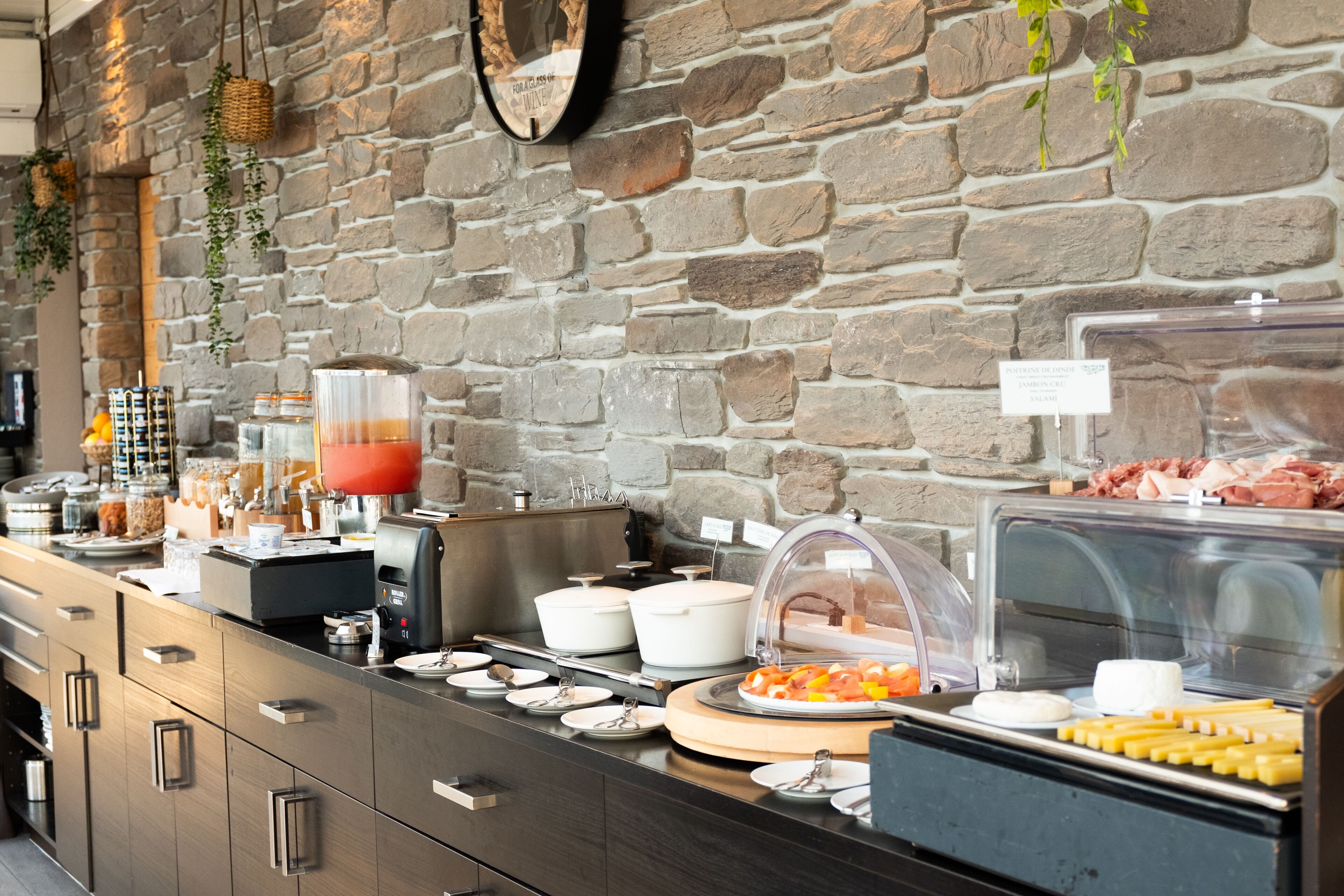 A buffet setup with various food items, a coffee machine, and a stone wall background.