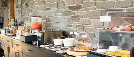 A buffet setup with various food items, a coffee machine, and a stone wall background.