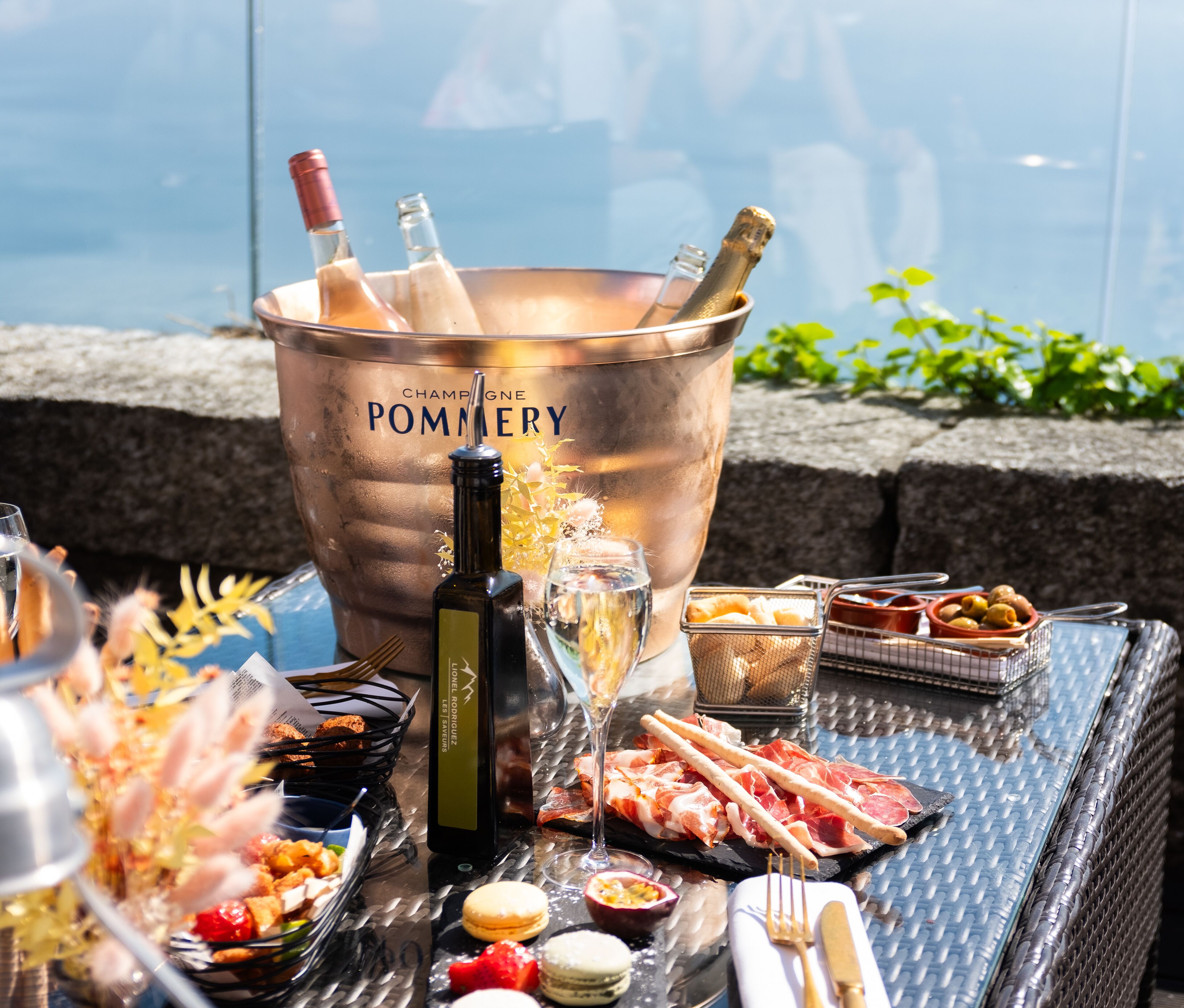 Un balde de champán con botellas y copas, diversos aperitivos y vistas al agua.