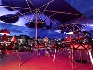 A rooftop terrace with multiple tables and chairs, umbrellas, and a city skyline in the background. - ibis Styles Lausanne Center Mad House (Lausanne)