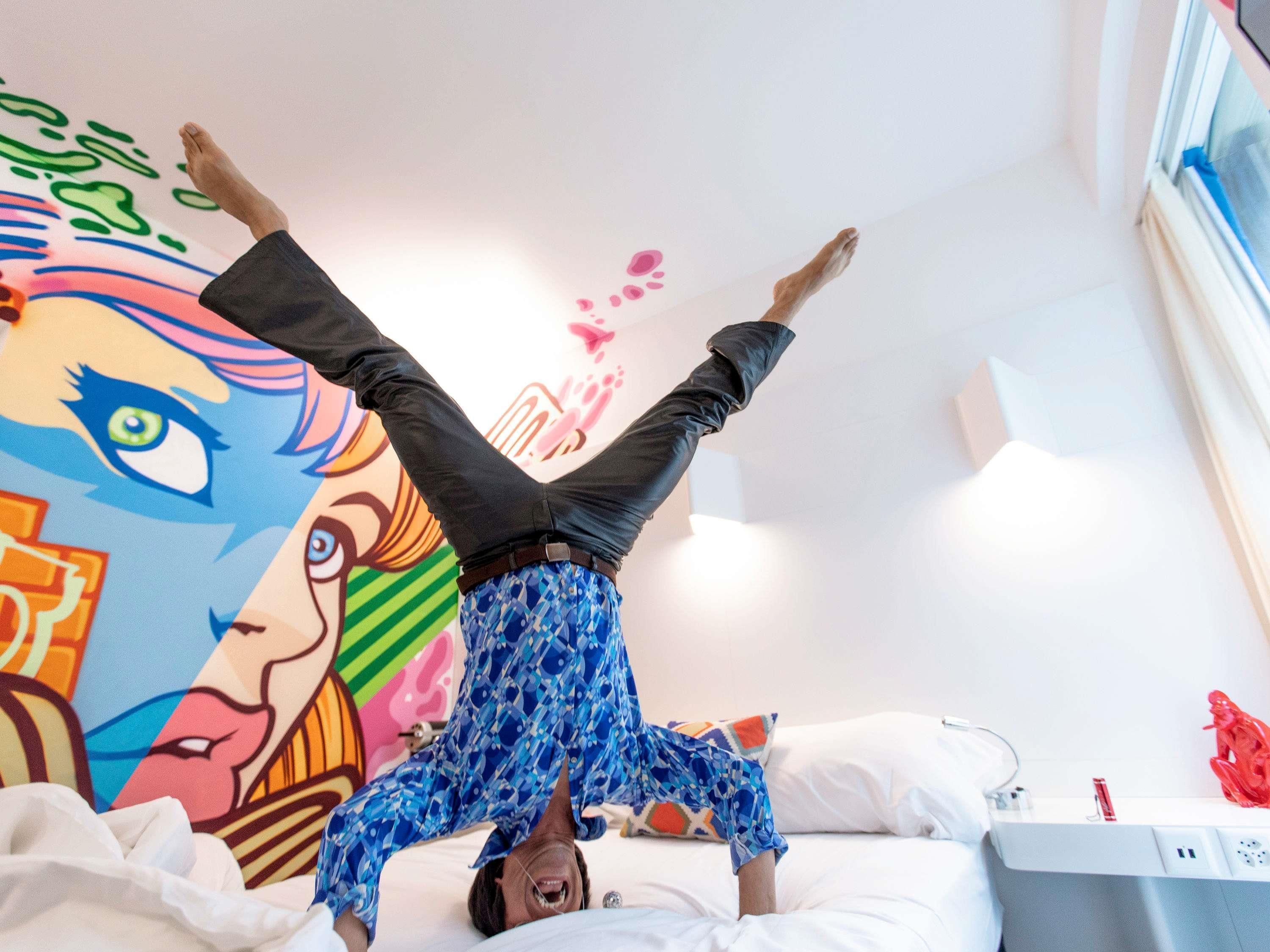 Una persona acostada en una cama en una habitación con un mural colorido en la pared.