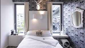 Ein modernes Schlafzimmer mit Bett, Schreibtisch, Stuhl, einem Fenster mit Vorhängen, einer Wanddekoration und einem Spiegel.