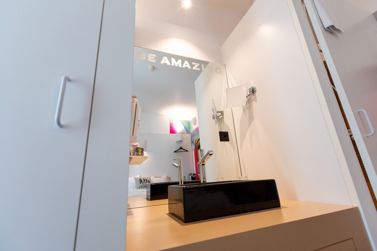 Een moderne badkamer met een grote spiegel, een zwart rechthoekig object op het aanrecht en een handdoekhouder.