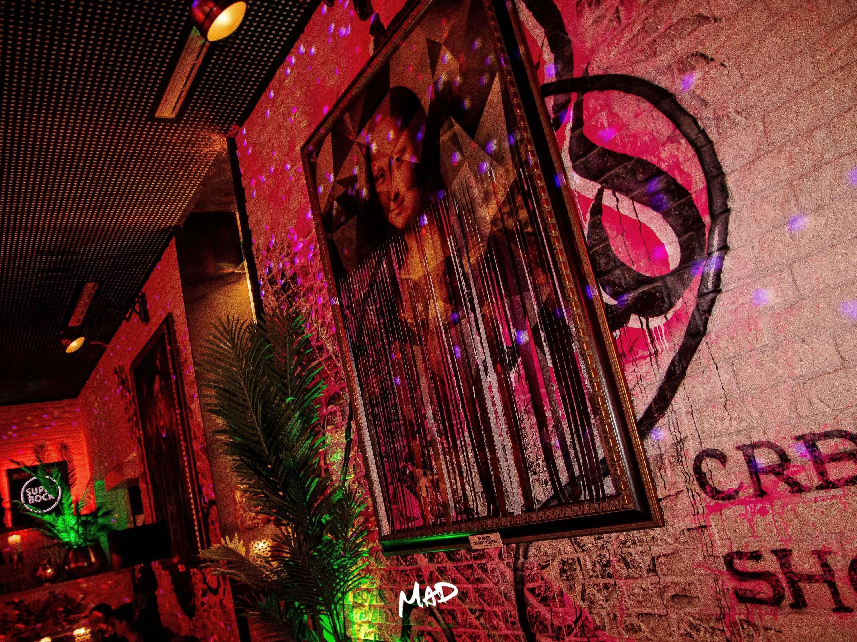 A dimly lit bar area with a graffiti wall, a framed picture, and a neon sign.
