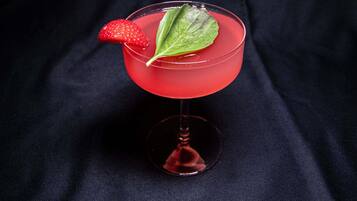 Un cocktail servi dans un verre à pied, garni d’une fraise et d’une feuille, le tout présenté sur un fond sombre.