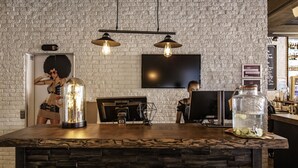 Eine Bar mit einer Steintheke, hängenden Pendelleuchten, einem großen Einweckglastopf und einem Flachbildfernseher an einer Ziegelwand.
