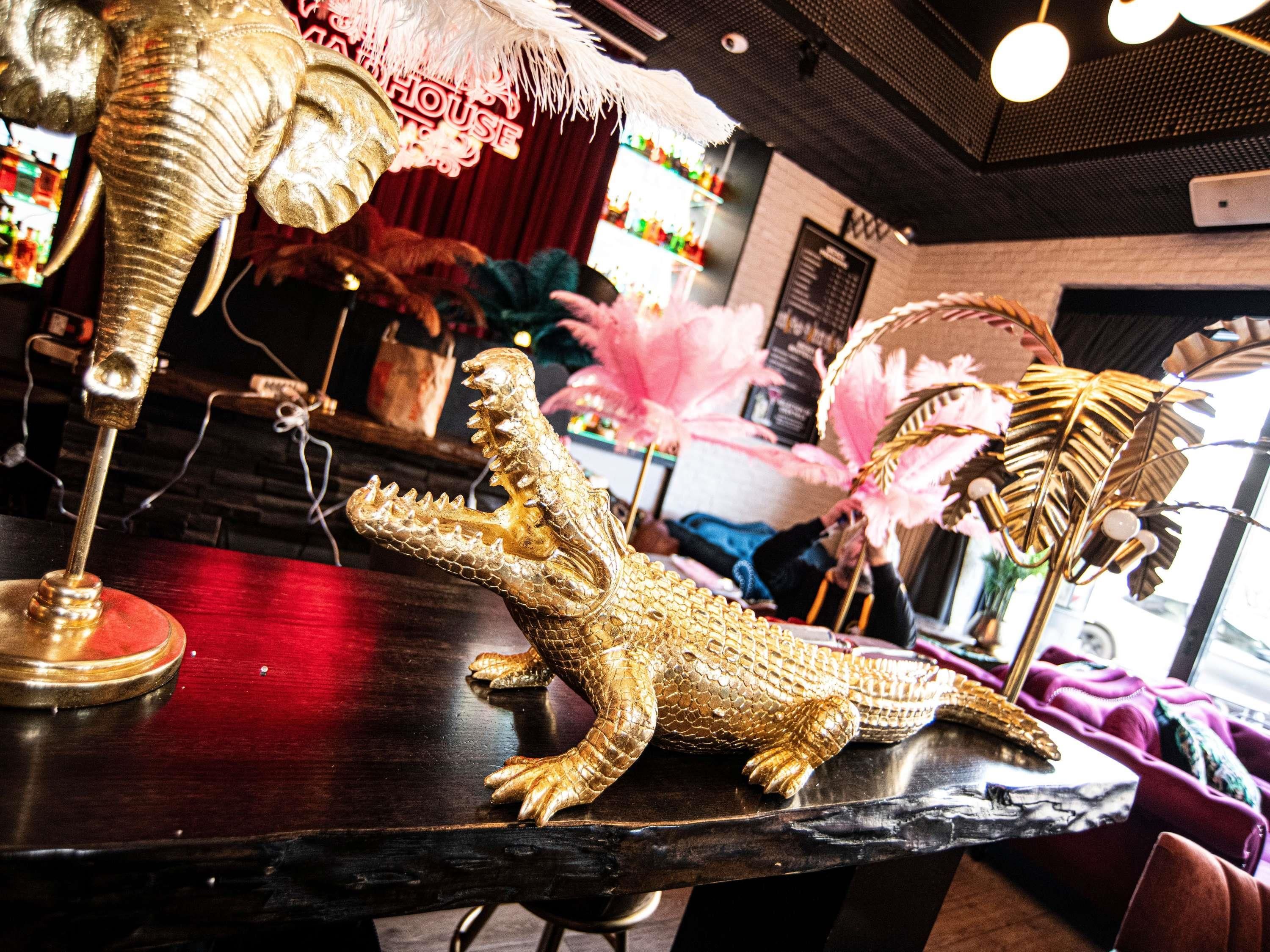 Una figurita de cocodrilo sobre una barra, una decoración de plumas y un letrero de neón en un bar.