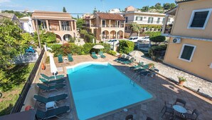 Una piscina con sillones de descanso y mesas, rodeada de edificios con balcones y un cielo despejado.