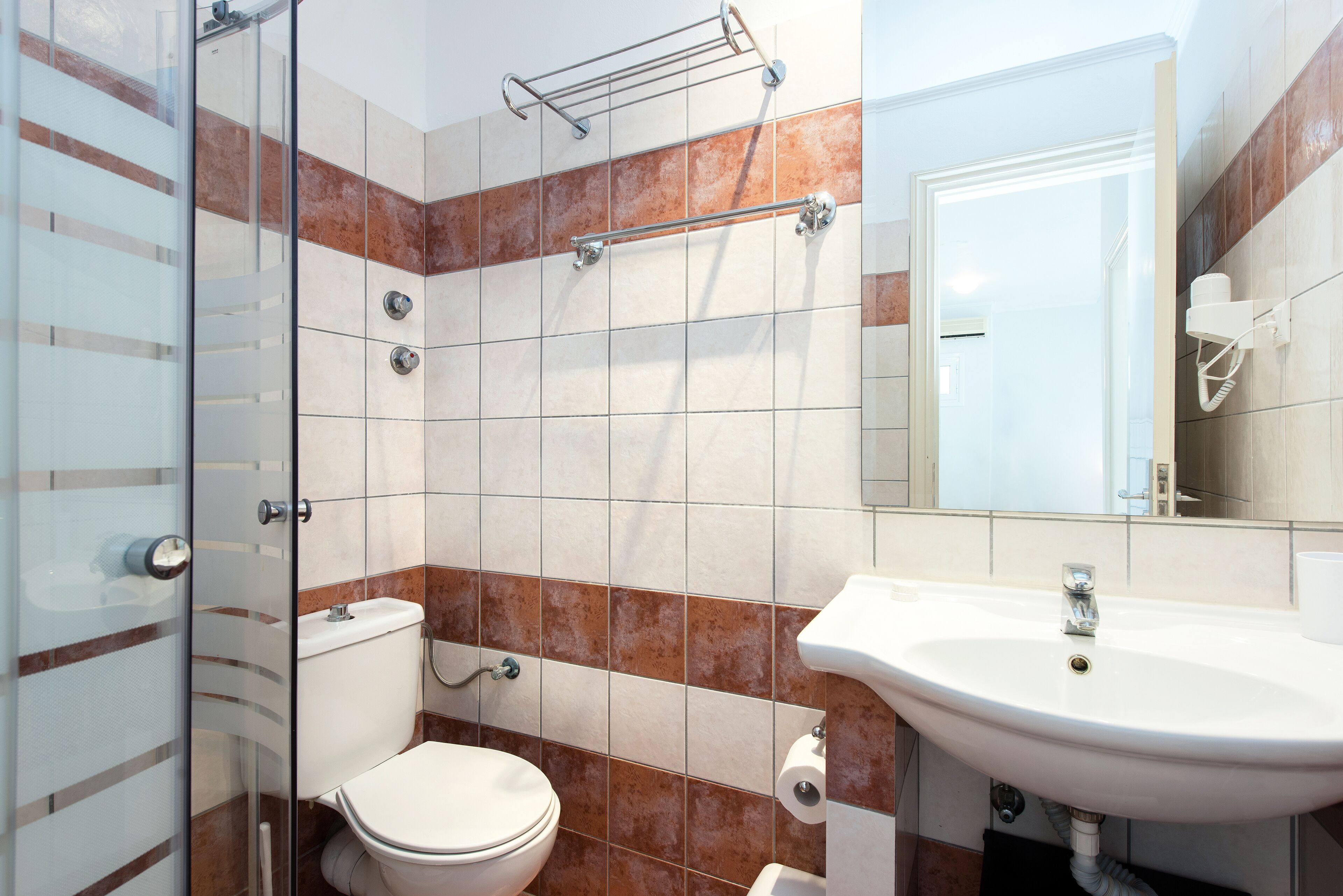 Un baño con cabina de ducha de vidrio, inodoro blanco, lavabo con espejo y toallero.