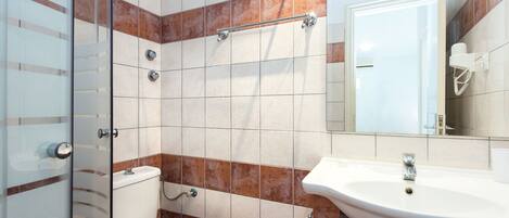 Un baño con cabina de ducha de vidrio, inodoro blanco, lavabo con espejo y toallero.