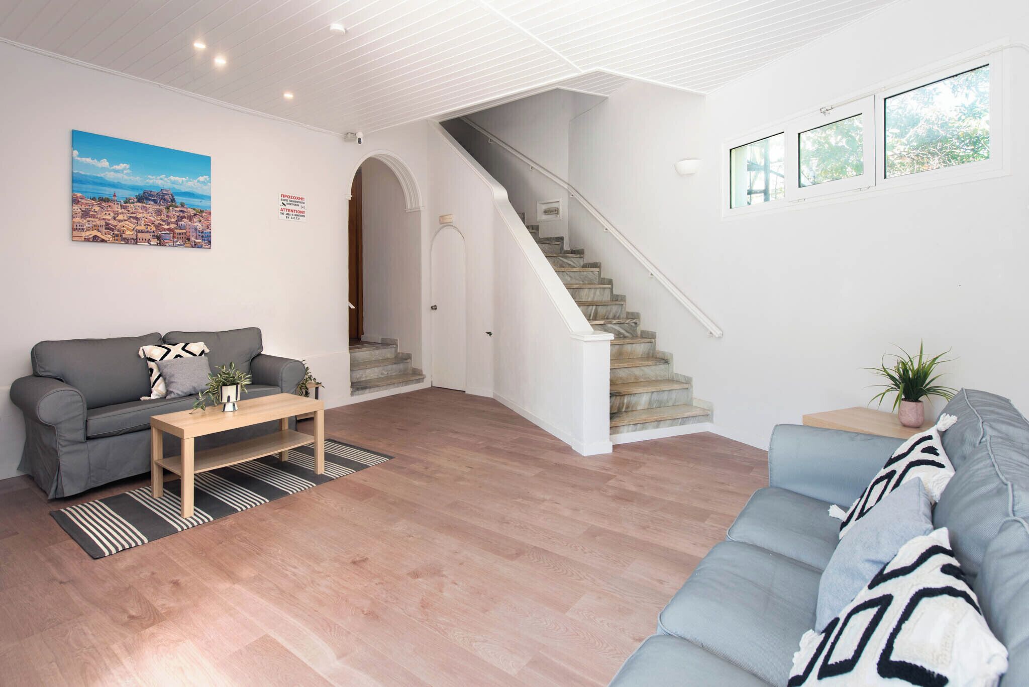 Ein Wohnzimmer mit grauem Sofa, einem Holztisch, einer Treppe und einem Stadtbild.